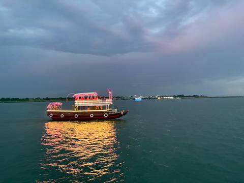       A boat on a river in the evening with lights reflecting on the water.
  