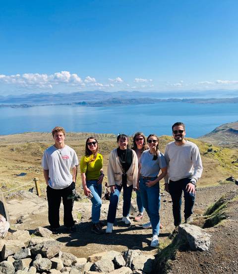       Group of people smiling with scenic cliffs and sea in the background.
  