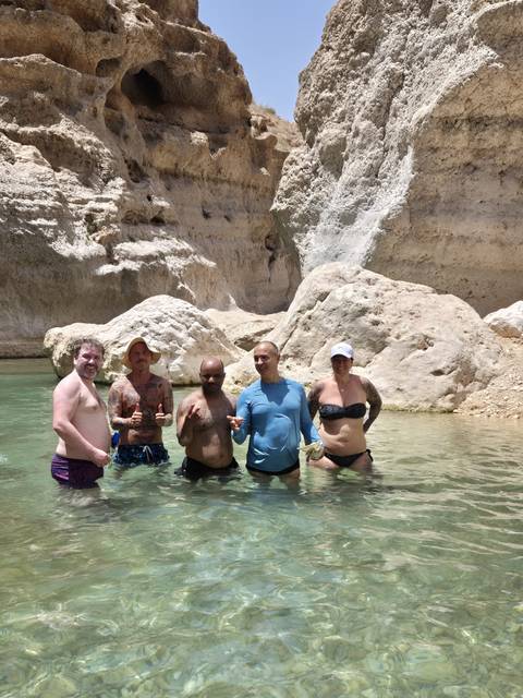       Group of people standing in clear water near rocky cliffs.
  