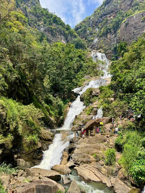 A waterfall surrounded by lush greenery with people walking on a path.