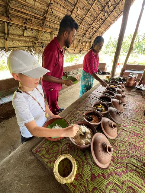 Child serving food from an array of dishes at an outdoor venue.