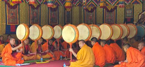 Monks in orange robes holding drums in a traditional setting.