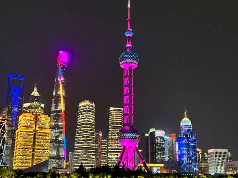 Night cityscape showing colorful illuminated skyscrapers, including the Oriental Pearl Tower in Shanghai.
