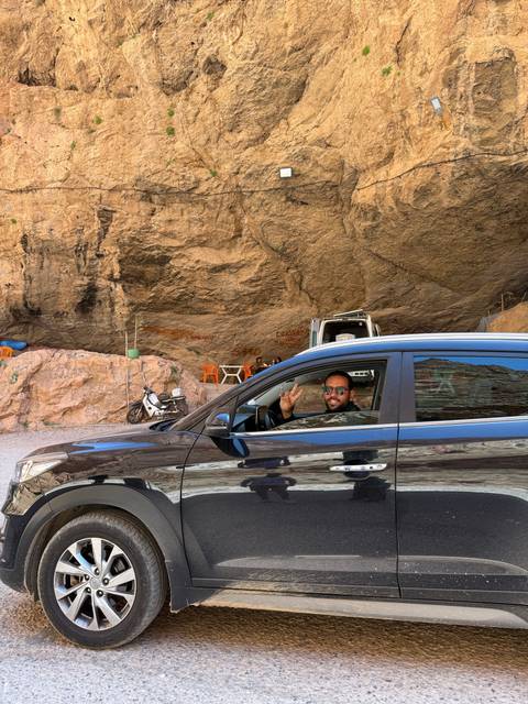       Man driving a car through a rocky area with a small seating area.
  