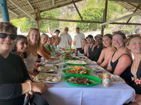       Large group of people seated at a long table with food.
  