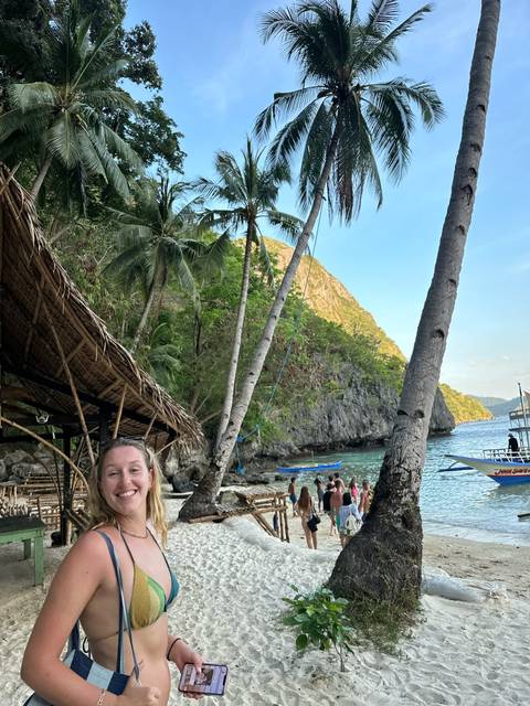       Smiling person in a tropical setting with palm trees.
  
