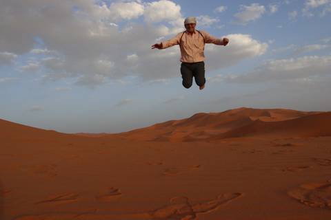 Person jumping in a desert with sand dunes.