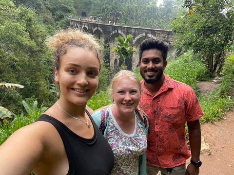 Three people with a bridge and greenery in the background.