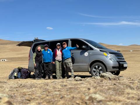       Group of people standing next to a van in a grassy plain.
  
