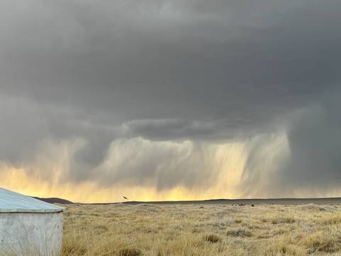       Rain clouds over a grassland with a distant hill.
  