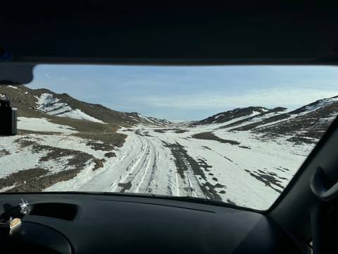       Snow-covered road through a valley, viewed from a vehicle.
  