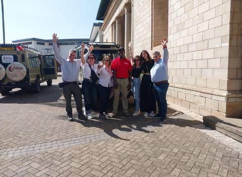       Group of people posing in front of safari vehicles, raising their hands in celebration.
  