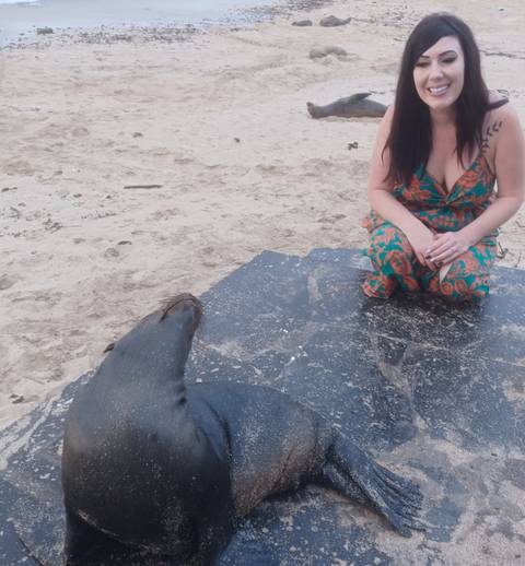 Person sitting with a sea lion on the beach.