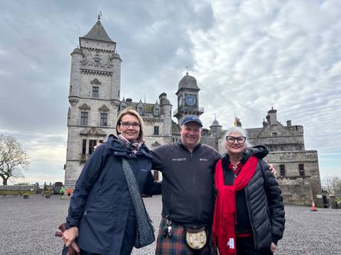Three people standing in front of a historic castle.
