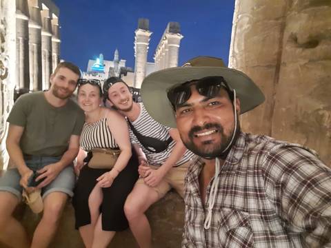 Group selfie at a monumental site during nighttime, with lit structures in the background.