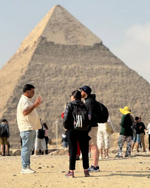      Tourists gathering with a pyramid in the background.
  