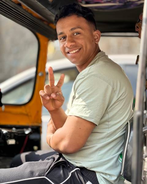       A person making a peace sign while sitting in an auto-rickshaw.
  
