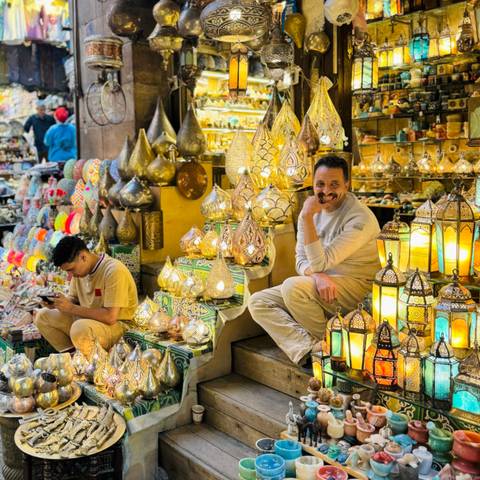       Two people among lanterns and colorful lights in a market setting.
  