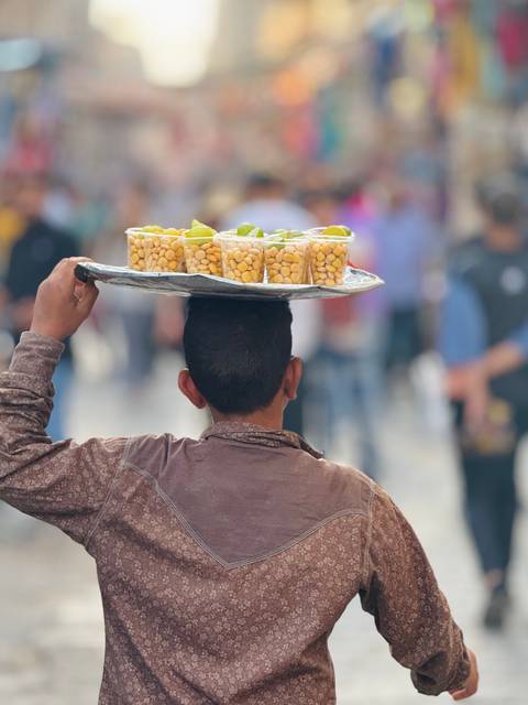       A person carrying cups of snacks on a tray balanced on their head.
  