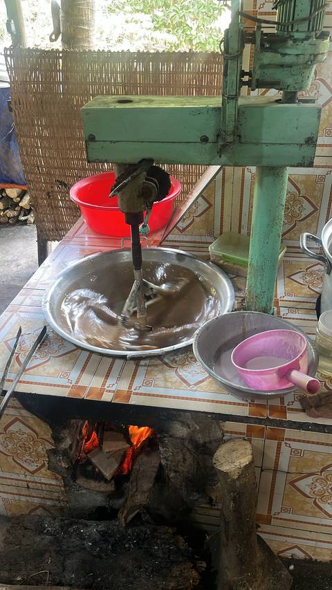 A large bowl with a mixer stirring a brown liquid substance on a table.