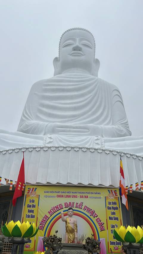       The lower section of a large white statue with decorative flags and carvings at its base.
  
