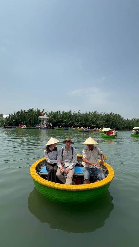 Group of people in traditional hats rowing a boat on a river.