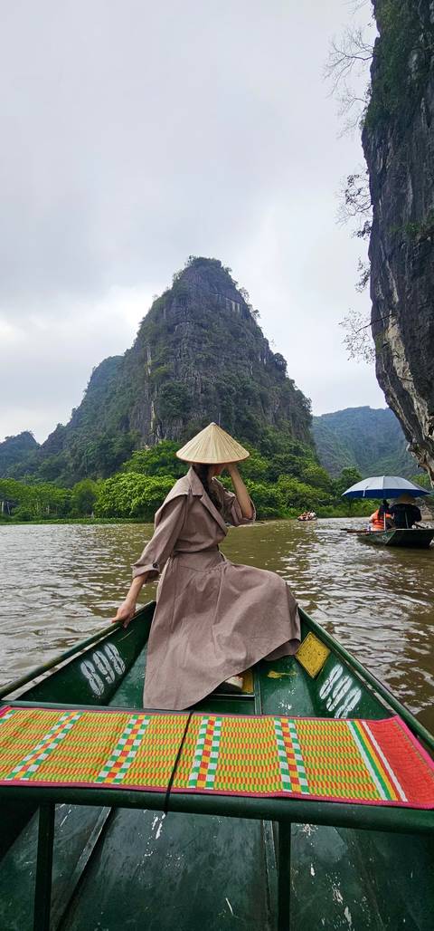 Person with a conical hat in a boat with karst mountains in the background.