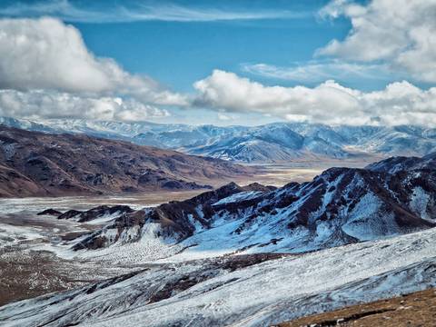 Panoramic view of mountainous terrain with snow and clouds.