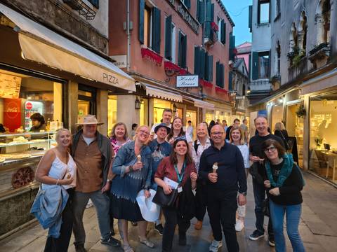 Group of people smiling in front of colorful buildings on a street at dusk.