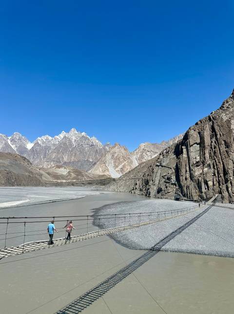 Suspension bridge over a river with mountain peaks in the background.