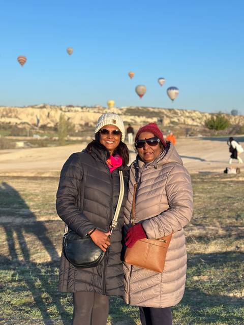 Two people bundled in jackets enjoy a scenic view with hot air balloons.