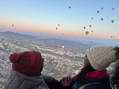 Hot air balloons over a vast landscape during sunrise with observers.