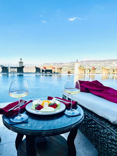       Two glasses of wine by a pool with a scenic mountain view.
  