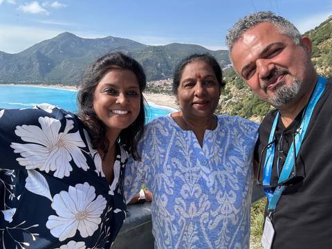 A group of three people smiling with a turquoise sea and mountains.