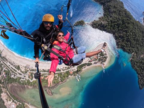      Two people paragliding over a coastal area with clear blue water.
  