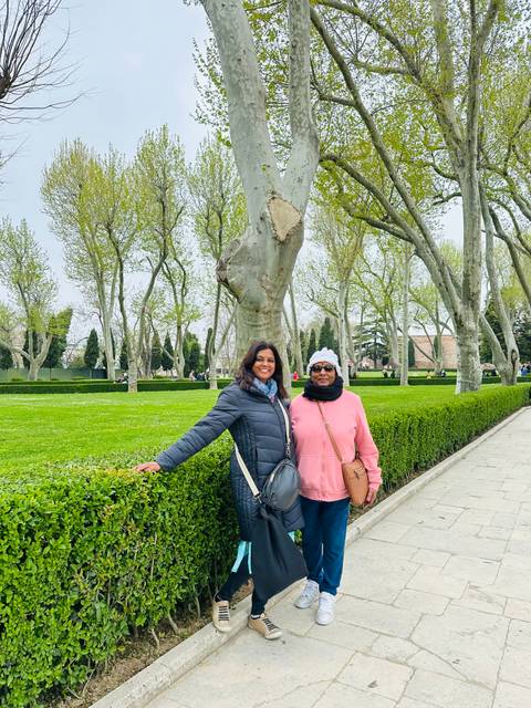       Two people posing in a well-maintained garden with trees.
  