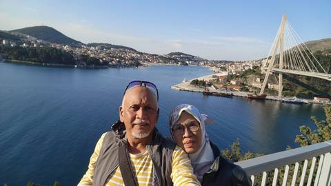 A couple taking a selfie with a body of water and a bridge in the background.
