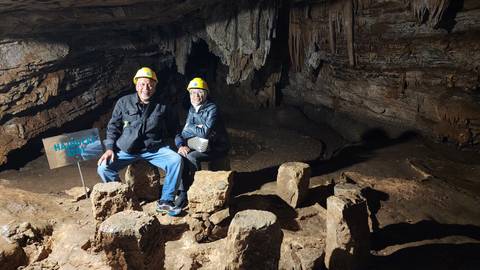 Two people wearing helmets inside a cave with a signpost.