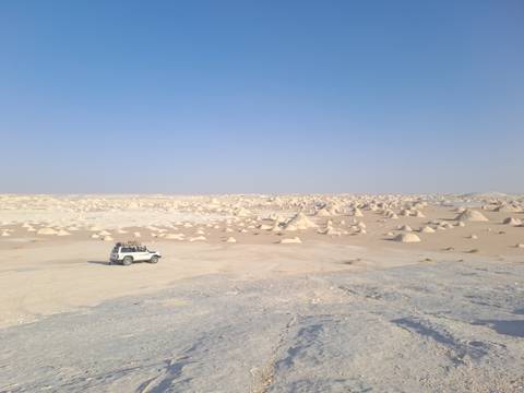 A white desert landscape with scattered rock formations and a vehicle.