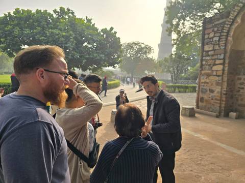 A tour group listening to a guide in a park area with ancient structures around.