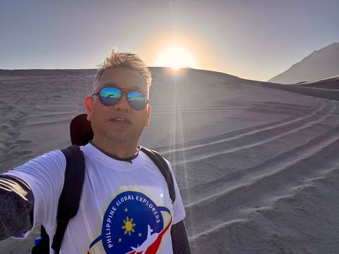 Man taking a selfie in a desert landscape with sunset.