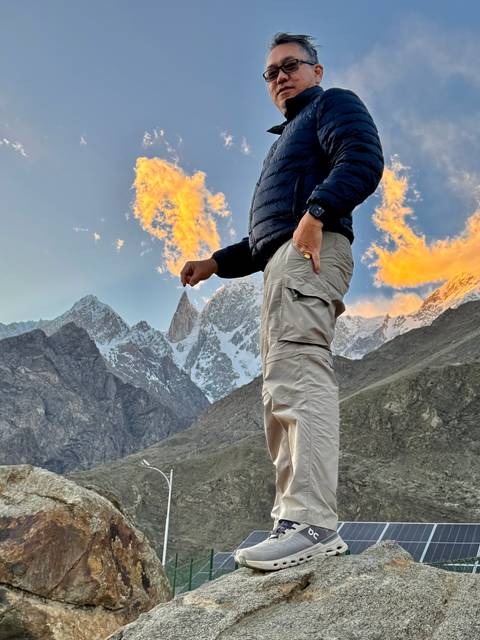       Man posing with mountains in the background during sunset.
  