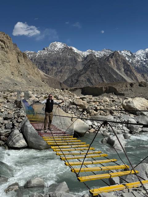       Man crossing a suspension bridge with rocky terrain.
  