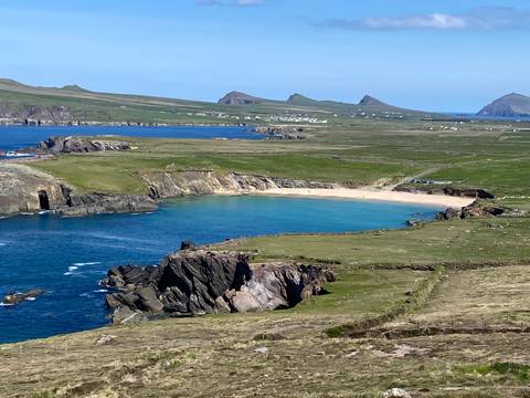       Scenic coastline with green fields and sandy beach.
  