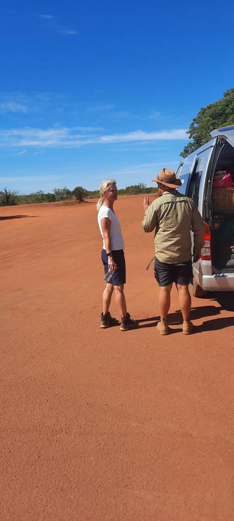 Two people standing next to a vehicle on a dirt road.