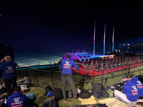       Audience at a night event with a stage setup near the water.
  