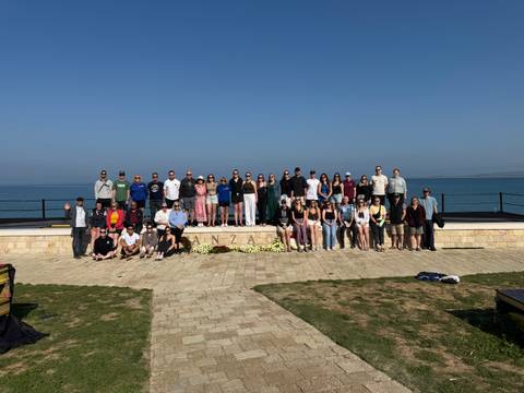       Large group of people posing together on a platform near the sea.
  
