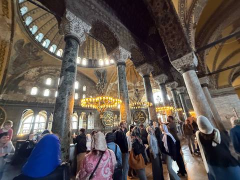       Interior of a grand mosque filled with people.
  