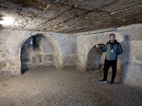 Man standing in an ancient stone chamber with arched alcoves.