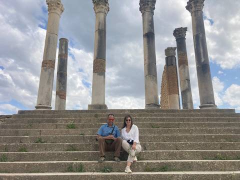Two people sitting on a stone staircase with ancient columns in the background.